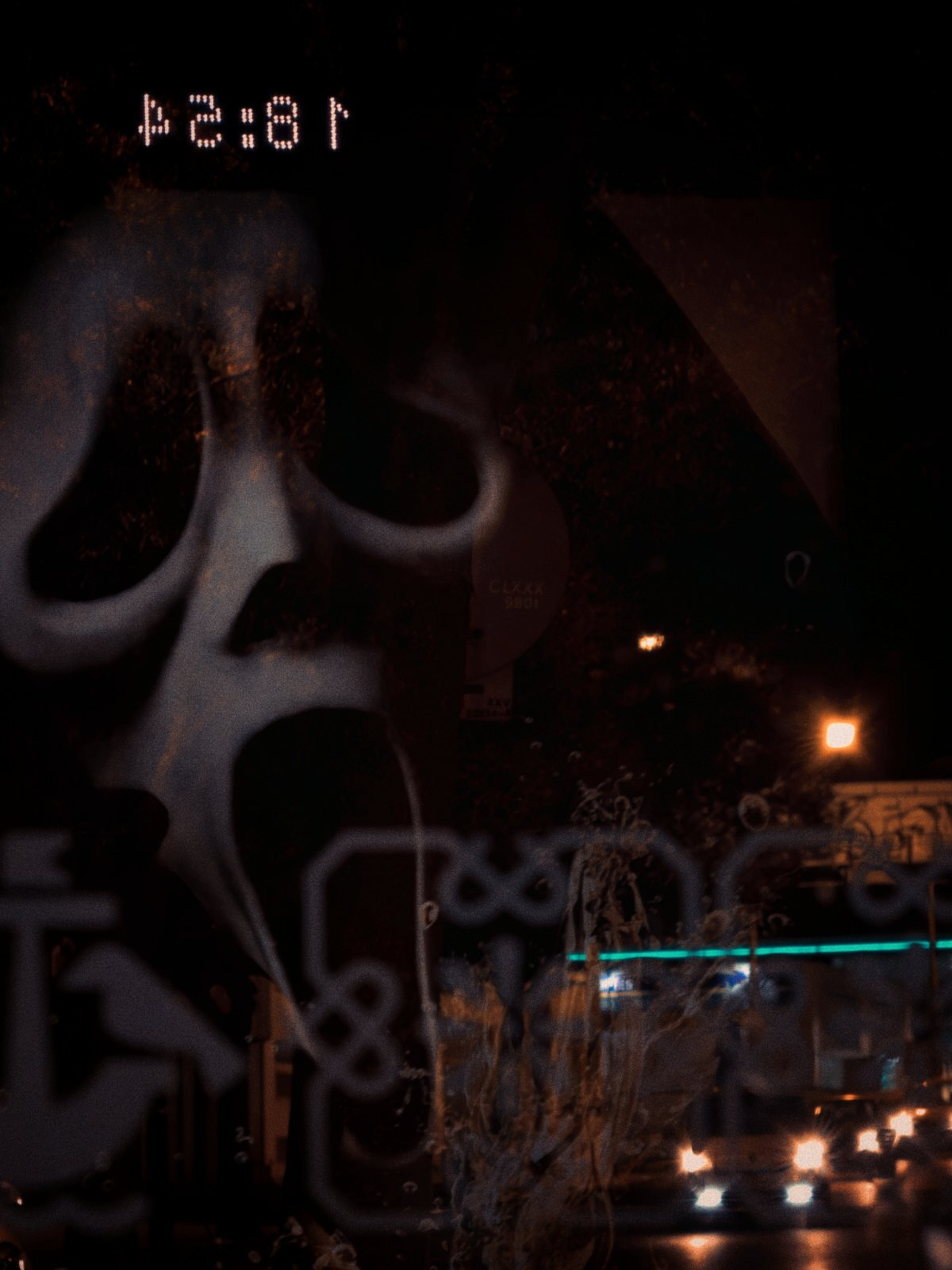 A ghostly, distorted face resembling the iconic Scream mask is reflected against a dark night backdrop with city lights and a digital clock reading 18:54.