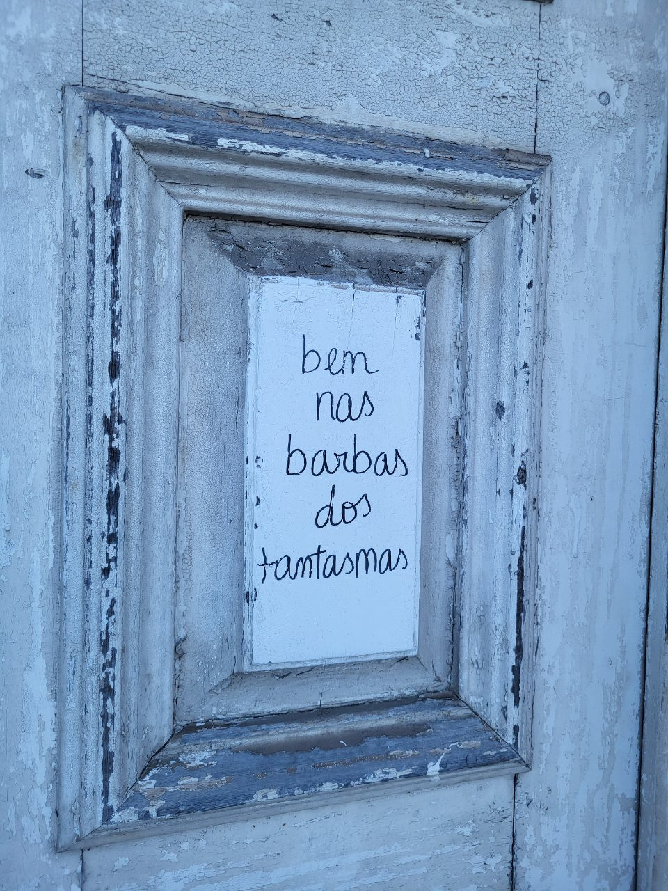 &ldquo;Bem nas barbas dos fantasmas&rdquo; written on an old white door. 