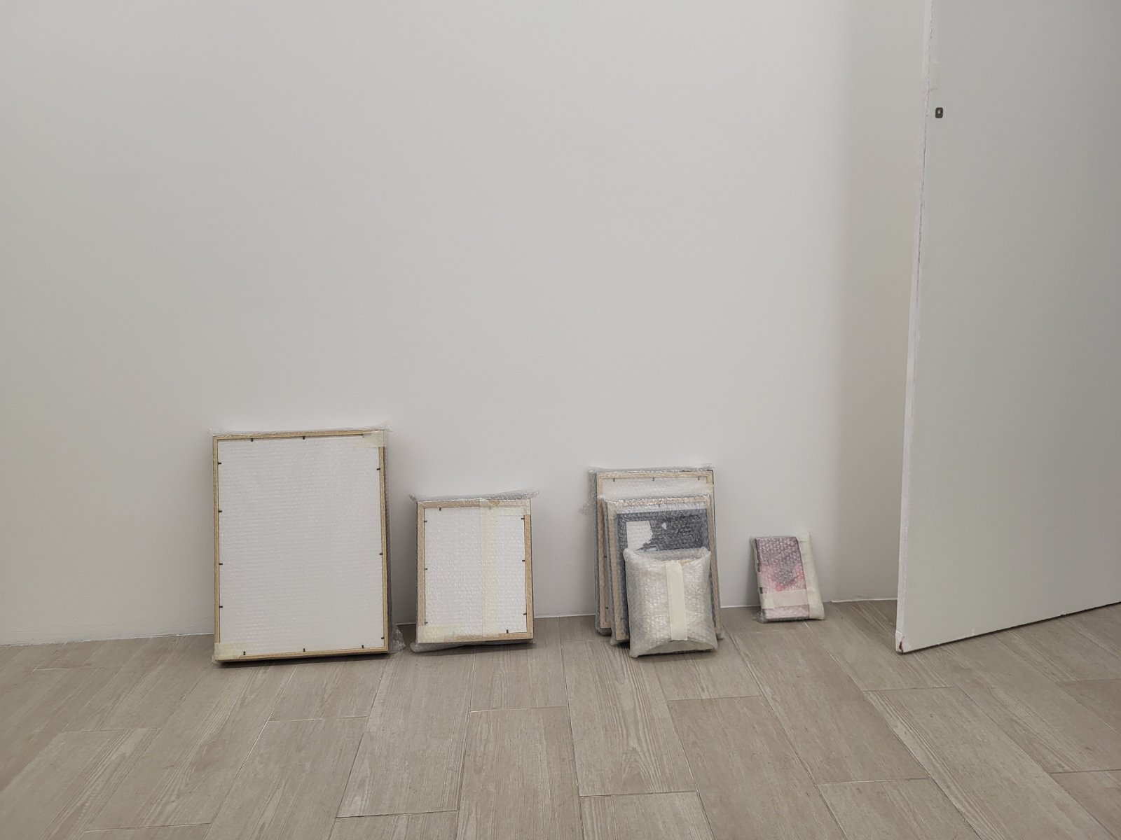 Several blank and wrapped canvases are stacked against a white wall on a tiled floor.