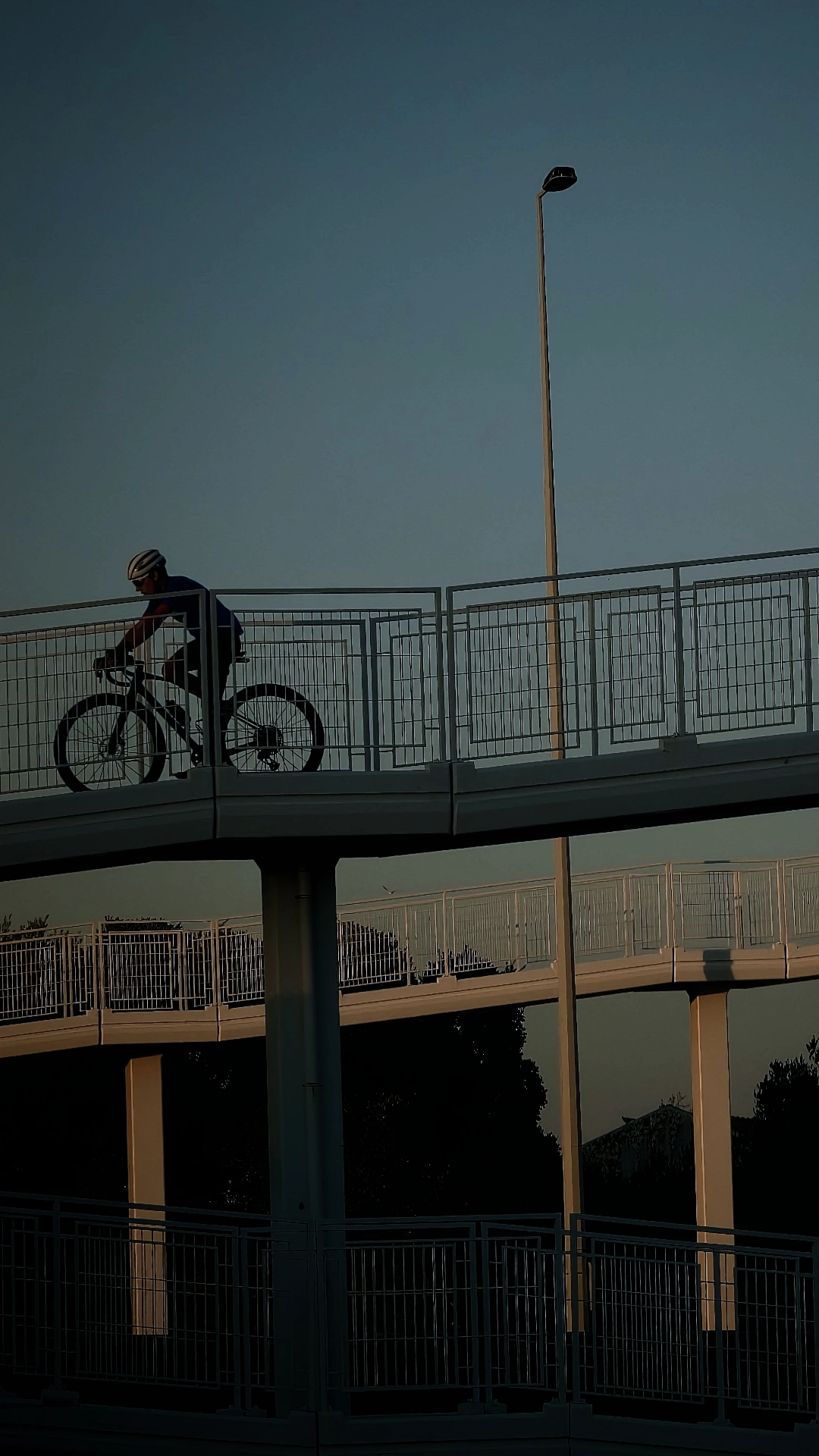 cyclist riding across an elevated pedestrian and bike bridge against a twilight sky