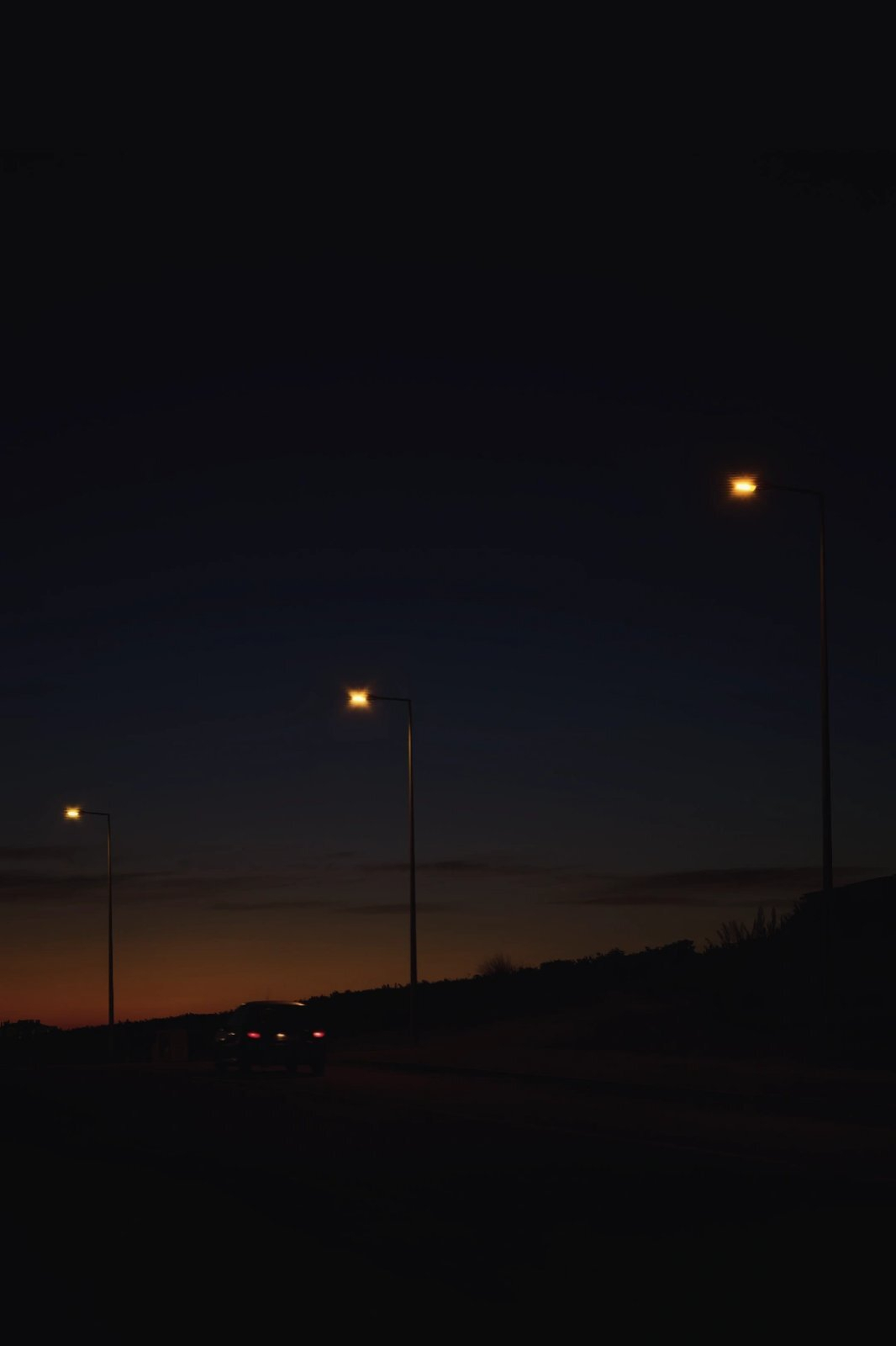 an empty road at twilight or dusk with illuminated streetlights and a silhouetted car in the distance
