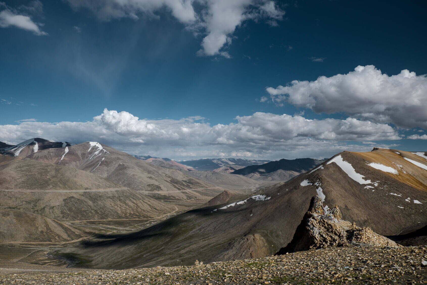 A vast mountainous landscape under a partly cloudy sky with patches of snow on the peaks.