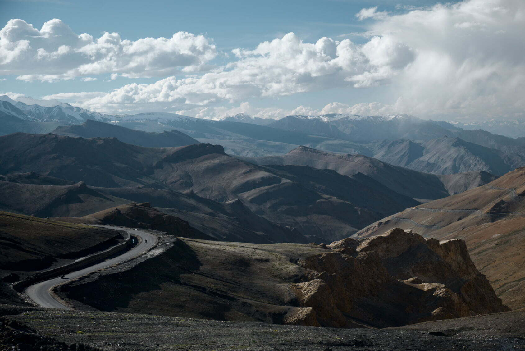 A winding road snakes through a vast mountainous landscape under a sky filled with scattered clouds.