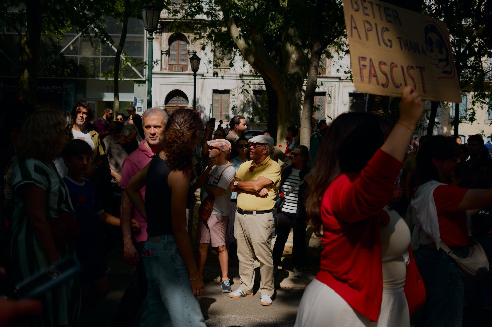 A group of people gather outdoors, and one person is holding a sign that reads BETTER A PIG THAN A FASCIST.