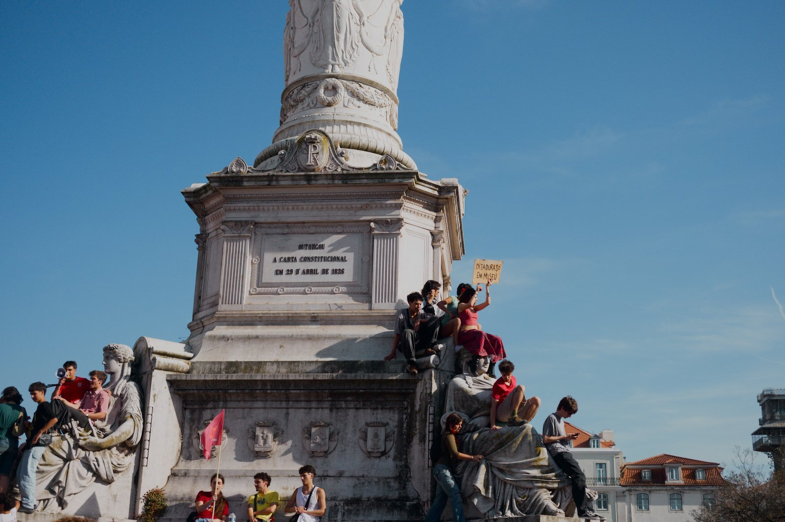 A group of people are gathered around a large stone monument with one person holding a sign during a clear day.