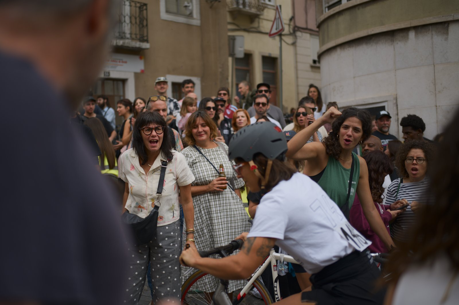 A crowd of people is watching and reacting to a cyclist riding past them on a street.