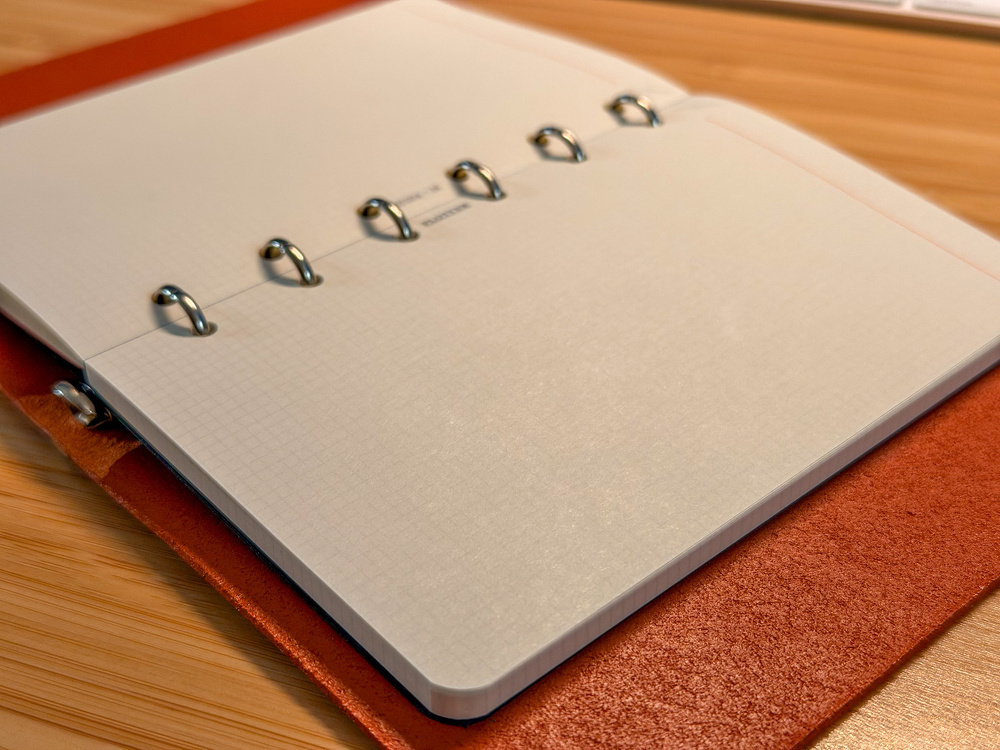 An open ring-bound notebook with graph paper pages is placed on a wooden surface.