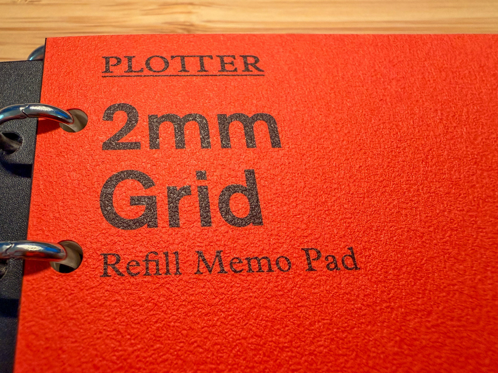 A red memo pad with PLOTTER, 2mm Grid, and Refill Memo Pad printed on the cover is shown with metal binder rings on the side.