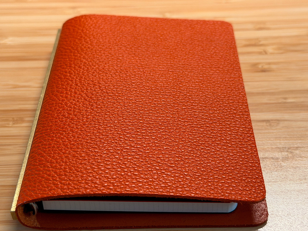 A closed, textured orange notebook with a gold-colored spine rests on a wooden surface.