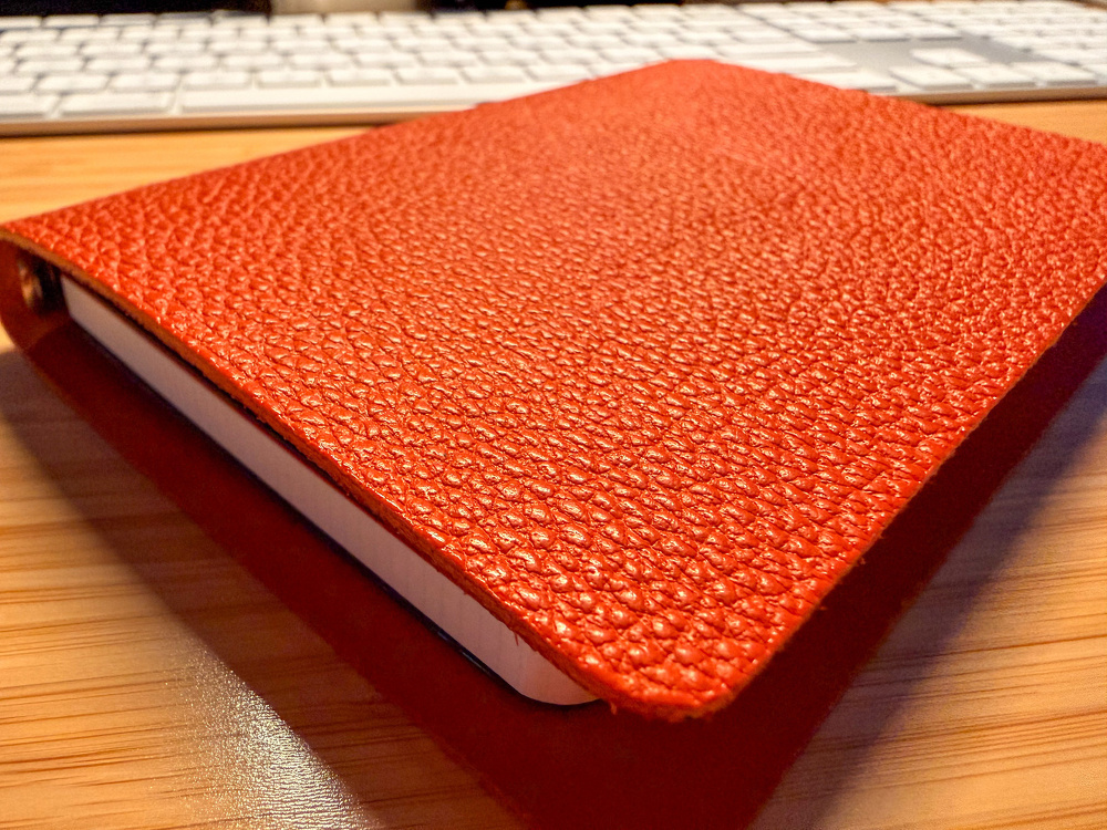 A textured red notebook is placed on a wooden desk in front of a computer keyboard.