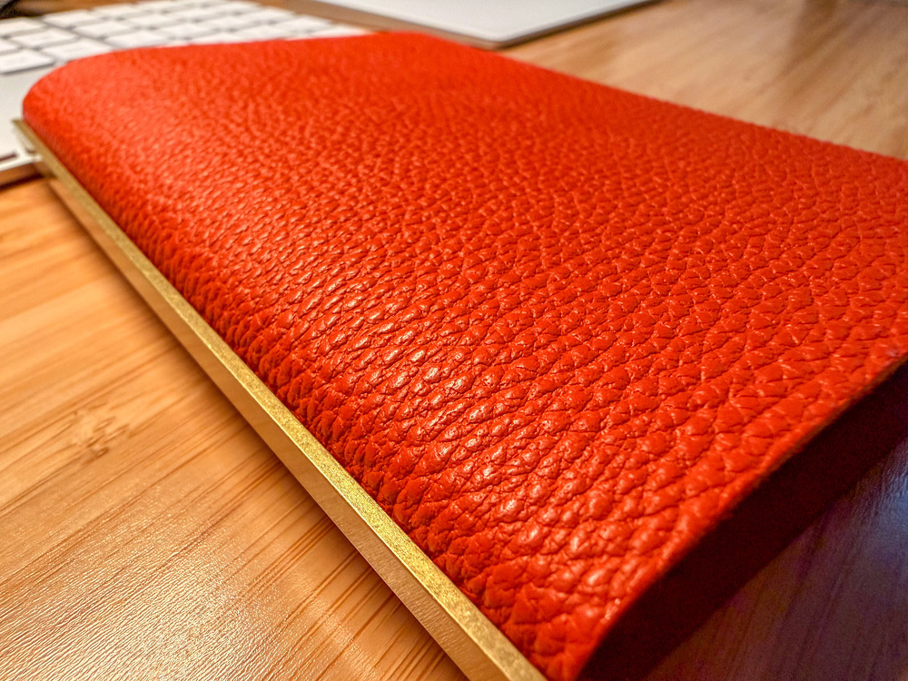 A red textured book or notebook is placed on a wooden surface near a computer keyboard.