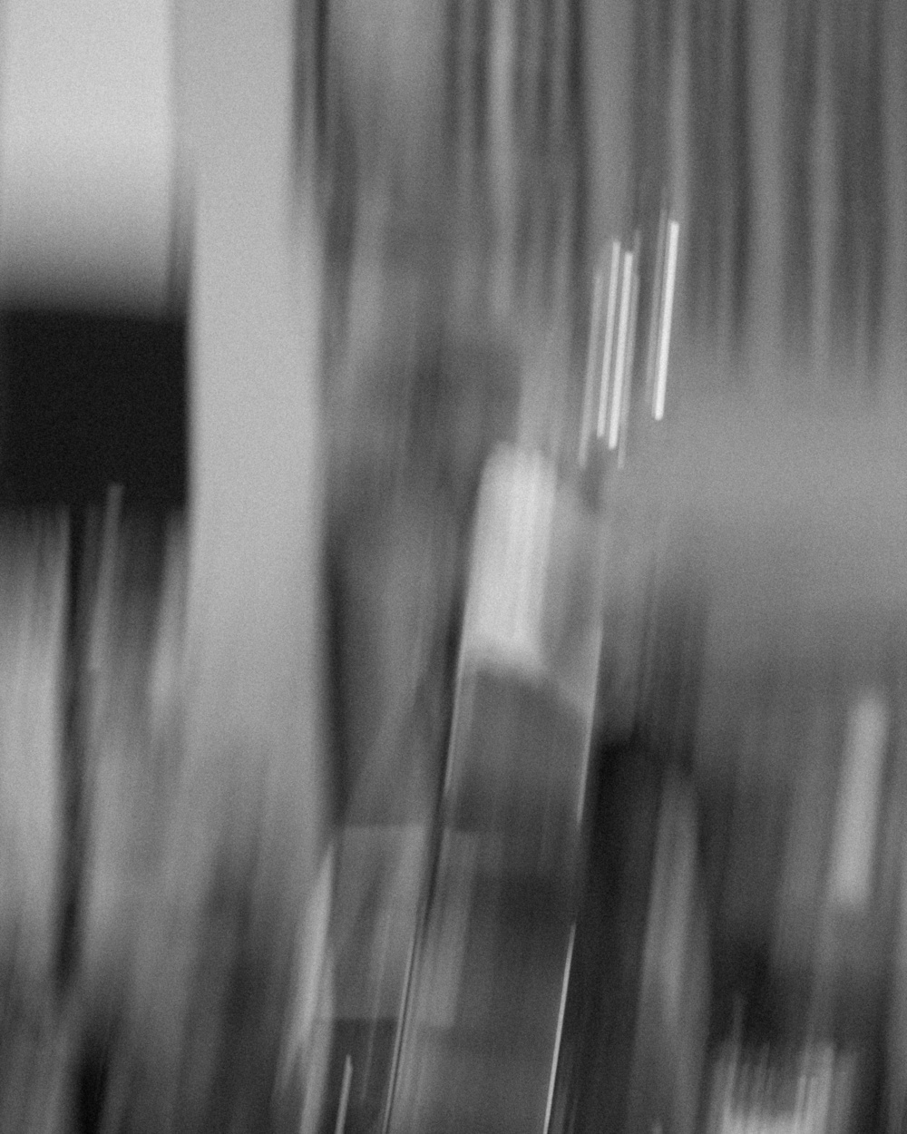 A blurred, abstract grayscale scene with vertical lines and indistinct shapes.