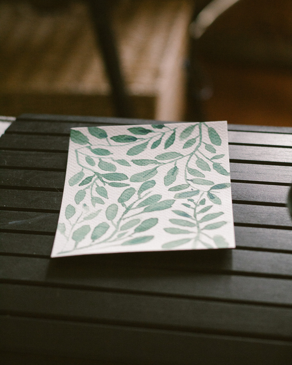 A piece of paper with a green leafy pattern lies on a dark-striped surface.