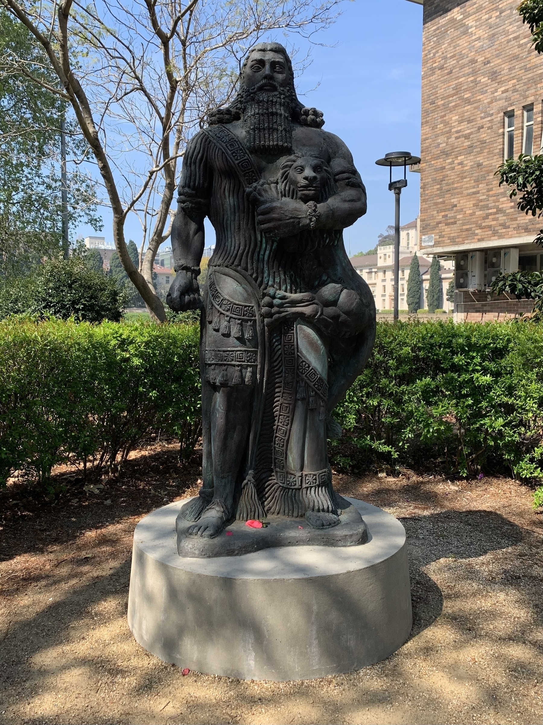 Metal statue on a concrete base. Statue is of a muscular, human-sized god/man dressed like a warrior king, grasping a lion in a headlock under his left arm