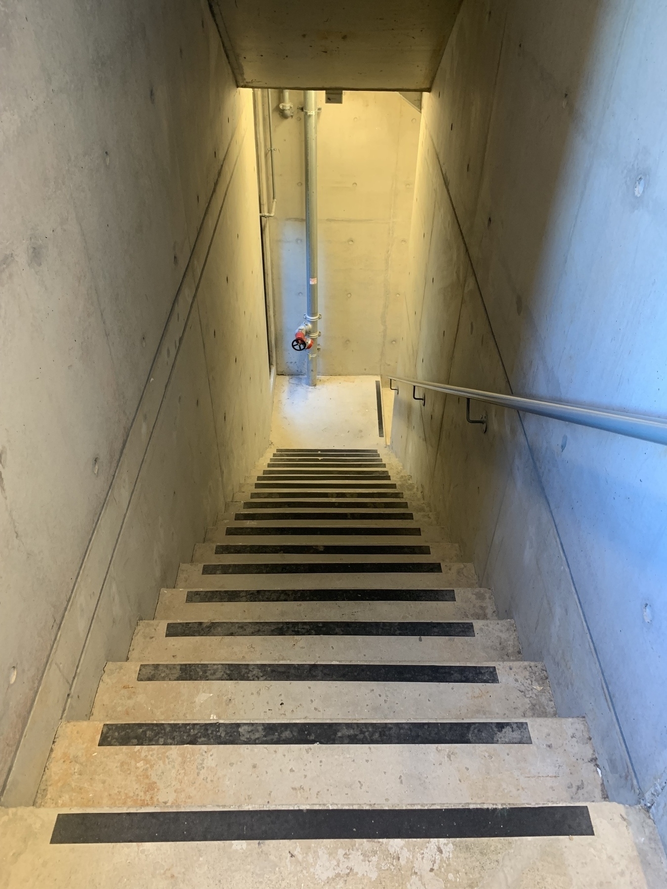 Looking down a flight of stairs with anti-slip grip strips, all within a concrete fire escape stairwell
