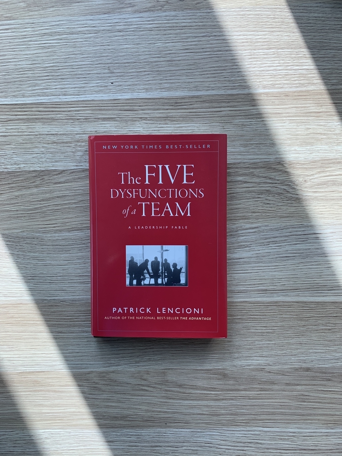 A red book (The Five Dysfunctions of a Team) on my desk with two strips of sunlight either side of it