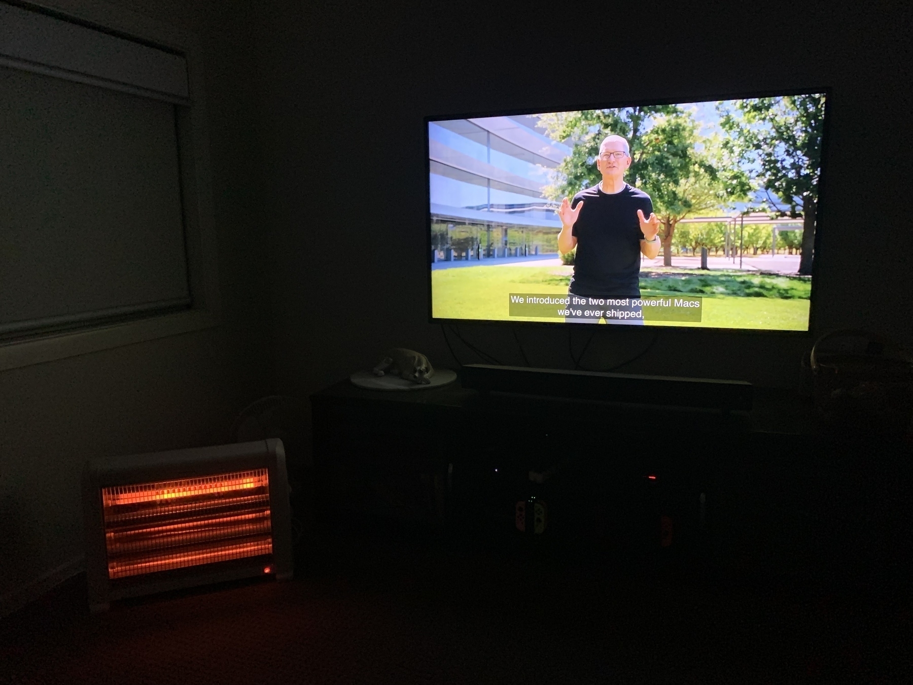A dark room illuminated only by the glow of an electric heater and a television showing Tim Cook presenting Apple’s September event.