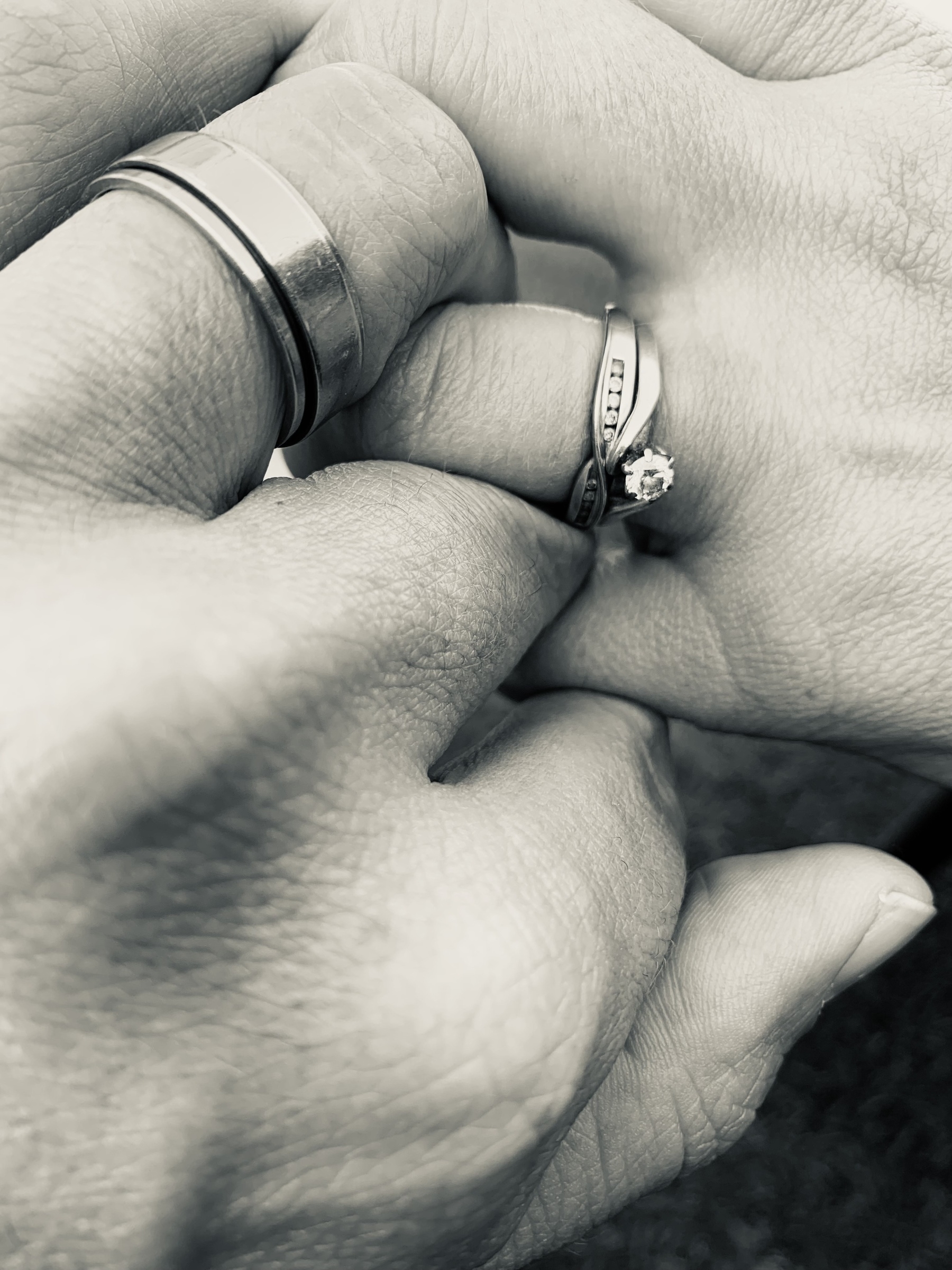 Black and white photo of two intertwined hands with rings on the ring fingers