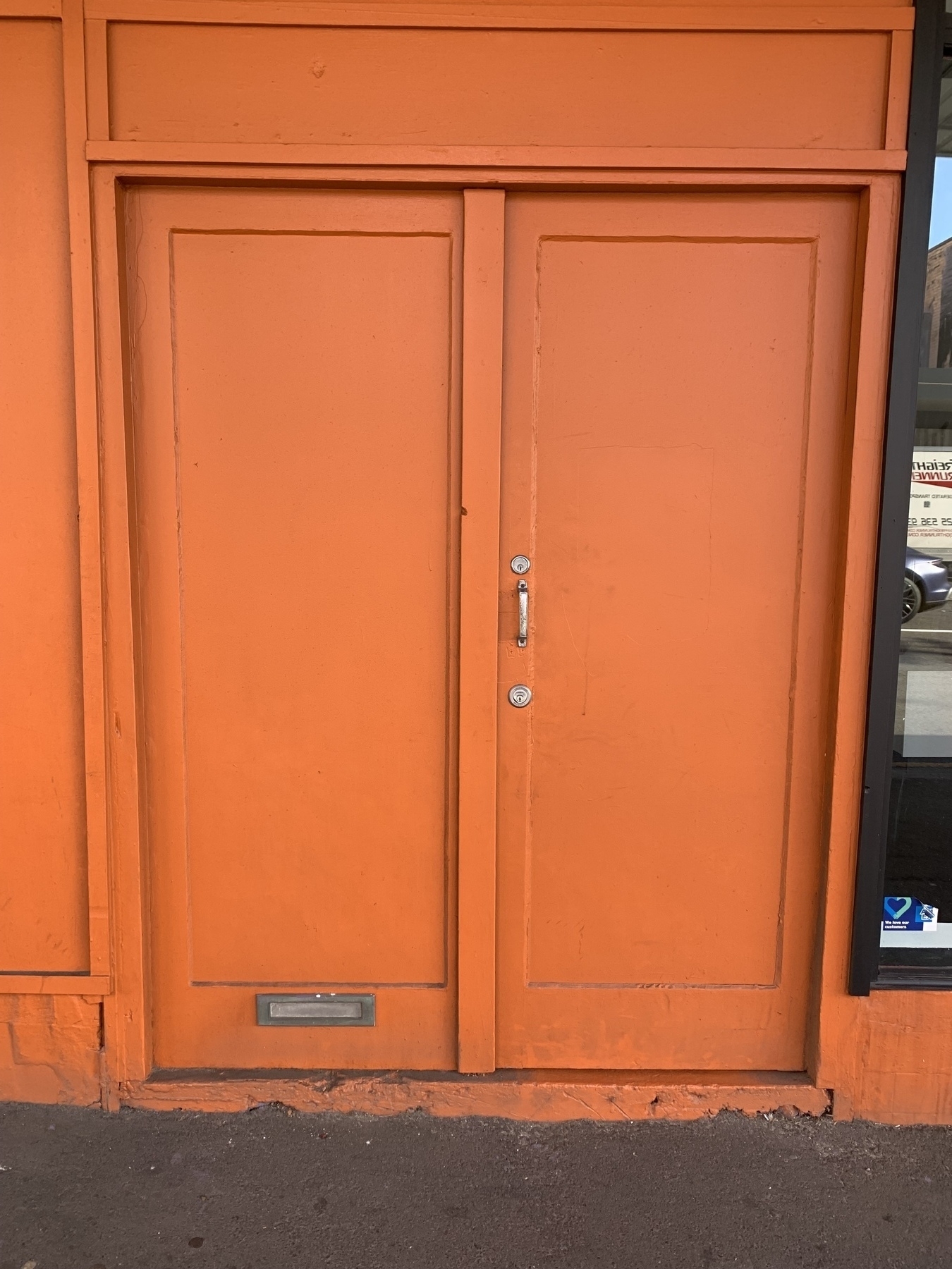 A double wooden door and door frame painted bright orange, with a mail slot at the very bottom of the left door