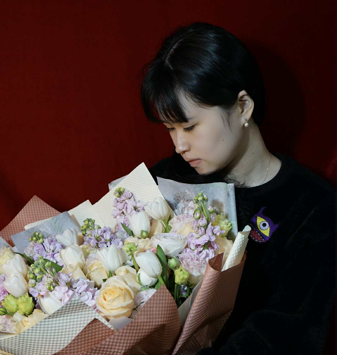 Auto-generated description: 一位女子低头看着一束精美的花束，背景是深红色。