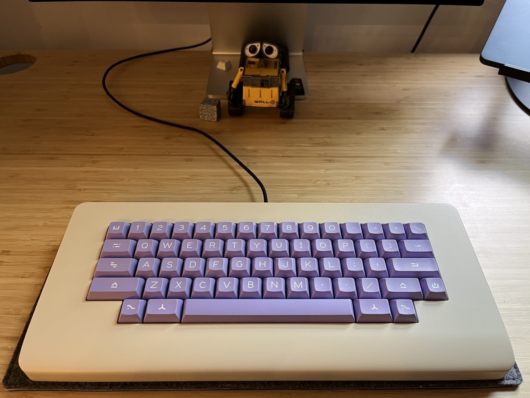 The Piggy mechanical keyboard on the Keebmat deskmat. The Piggy is on a bamboo colored desk. The little action figure of Walle is visible in the background.