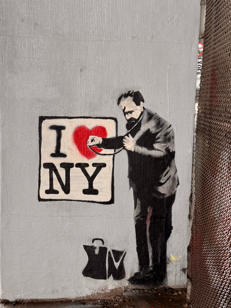 Graffiti of the I (heart) NY logo with a doctor checking the heart with a stethoscope. The doctor's old fashioned doctor's bag is open at his feet.