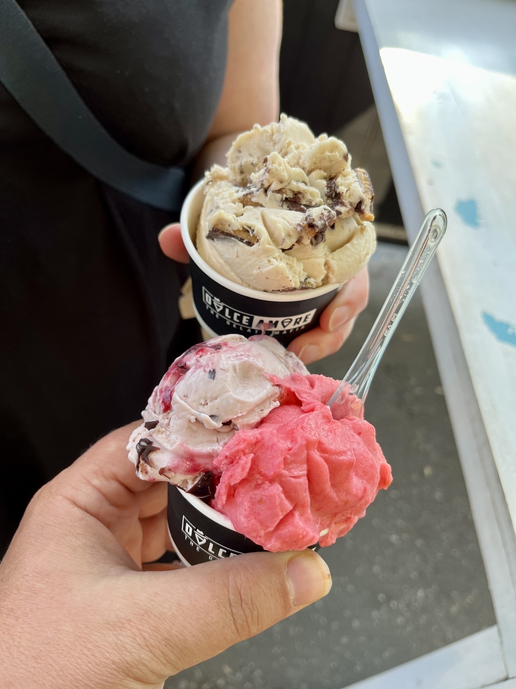 Hands holding two cups of ice cream. Peanut butter in the back, cherry mania and raspberry lemonade in the front. 