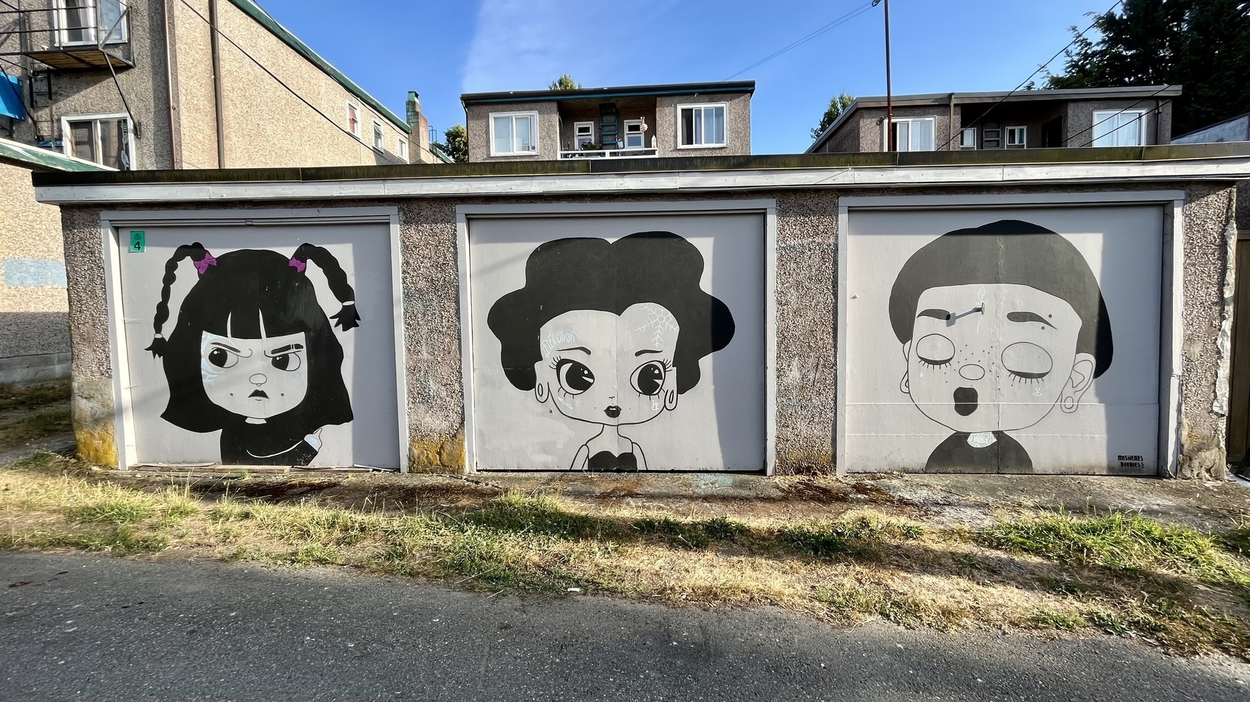 Murals of three female heads on garage doors in an alley 