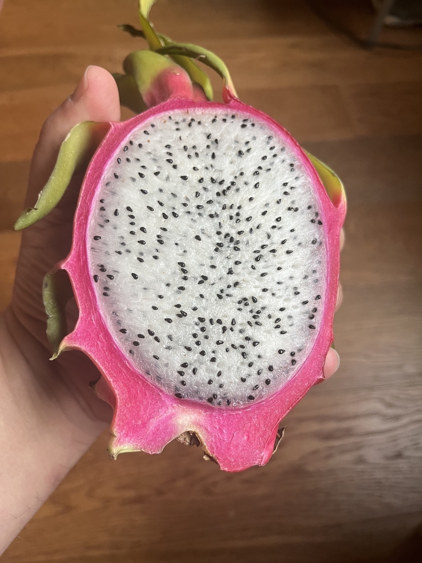 cut open side of a dragon fruit. White flesh small black seeds and the bright red skin of the fruit