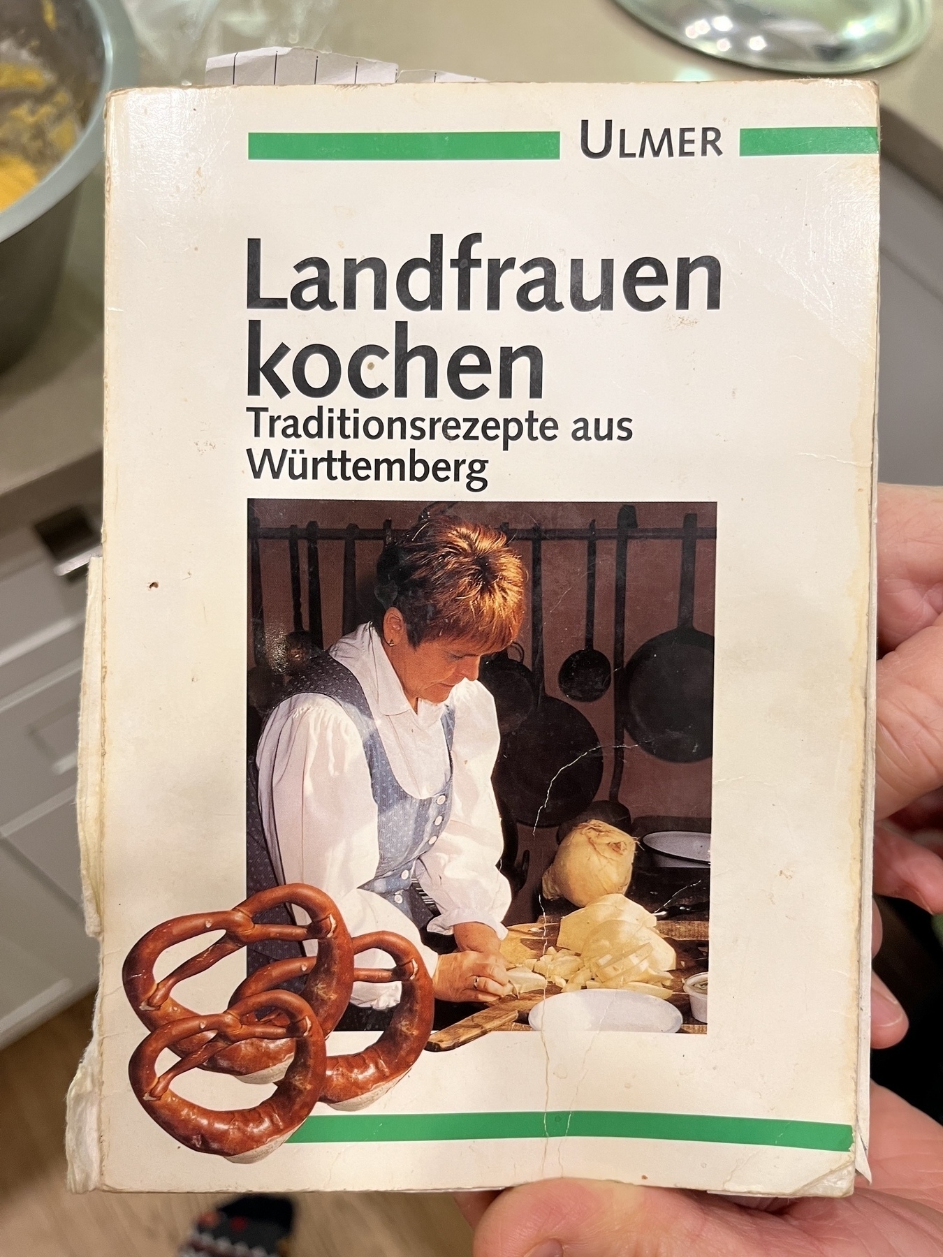 German cookbook titled “Landfrauen kochen - Traditionsrezepte aus Württemberg”&10;&10;A woman cooking with some pretzels pictured. 