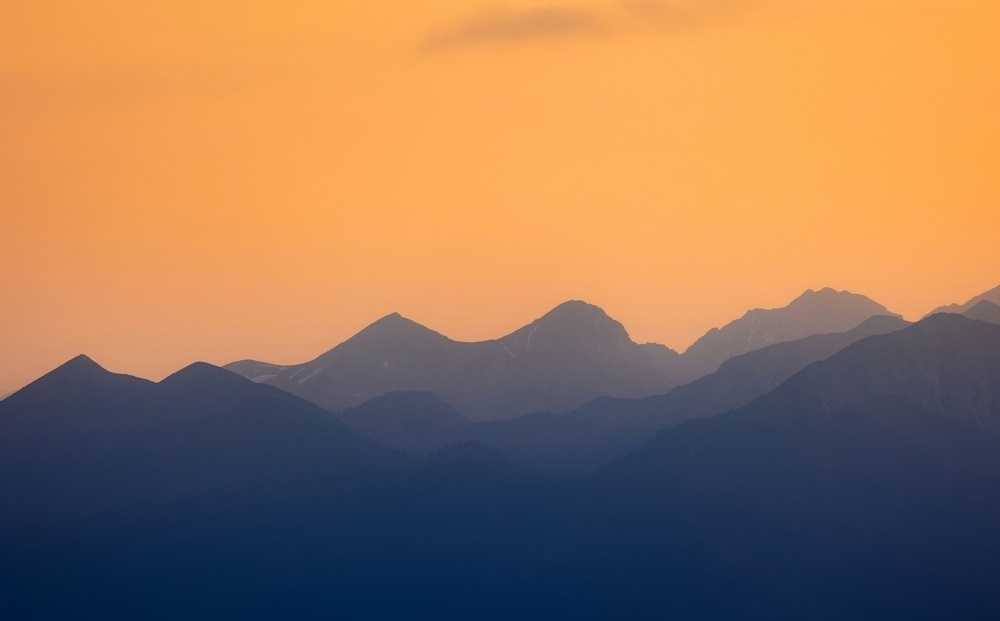 Silhouetted mountains stand against a warm, orange-hued sky at sunset.