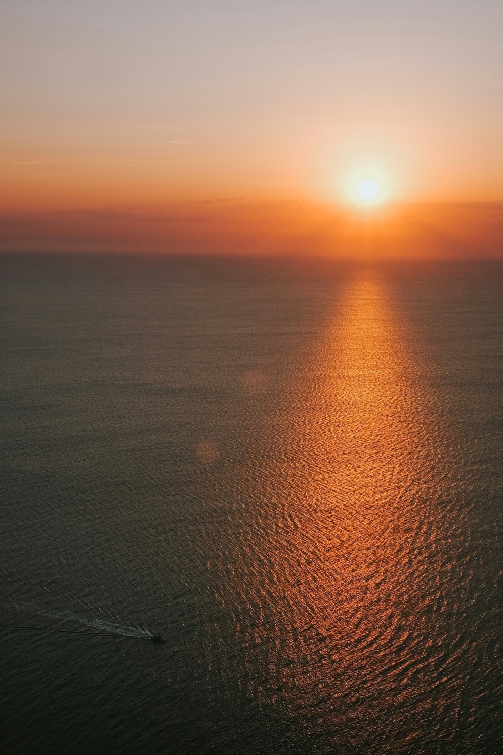 A serene sunset over the ocean creates a golden path of light on the water, with a small boat visible in the distance.