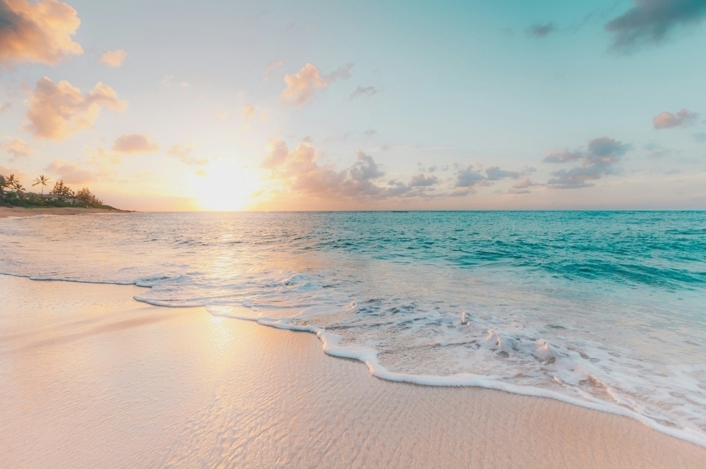 A serene beach scene with gentle waves lapping the shore under a vibrant sunset sky.