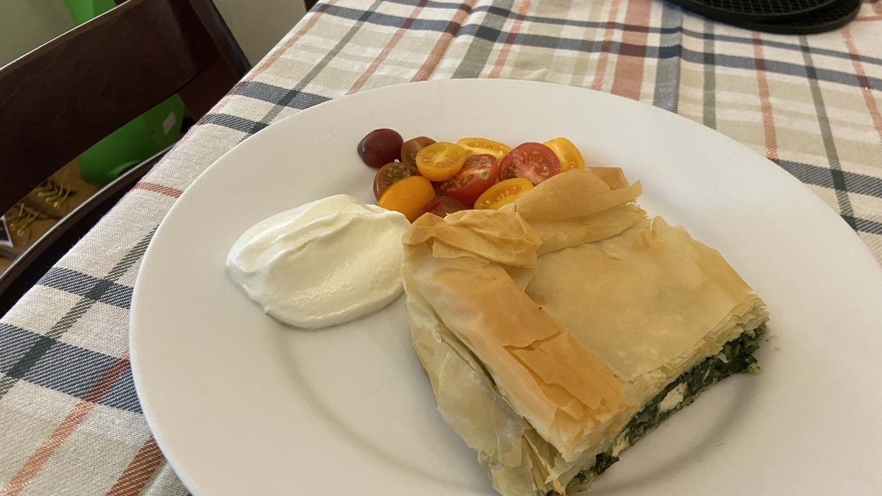 A plate with a slice of spinach pie, a dollop of cream, and a small side of colorful cherry tomatoes.