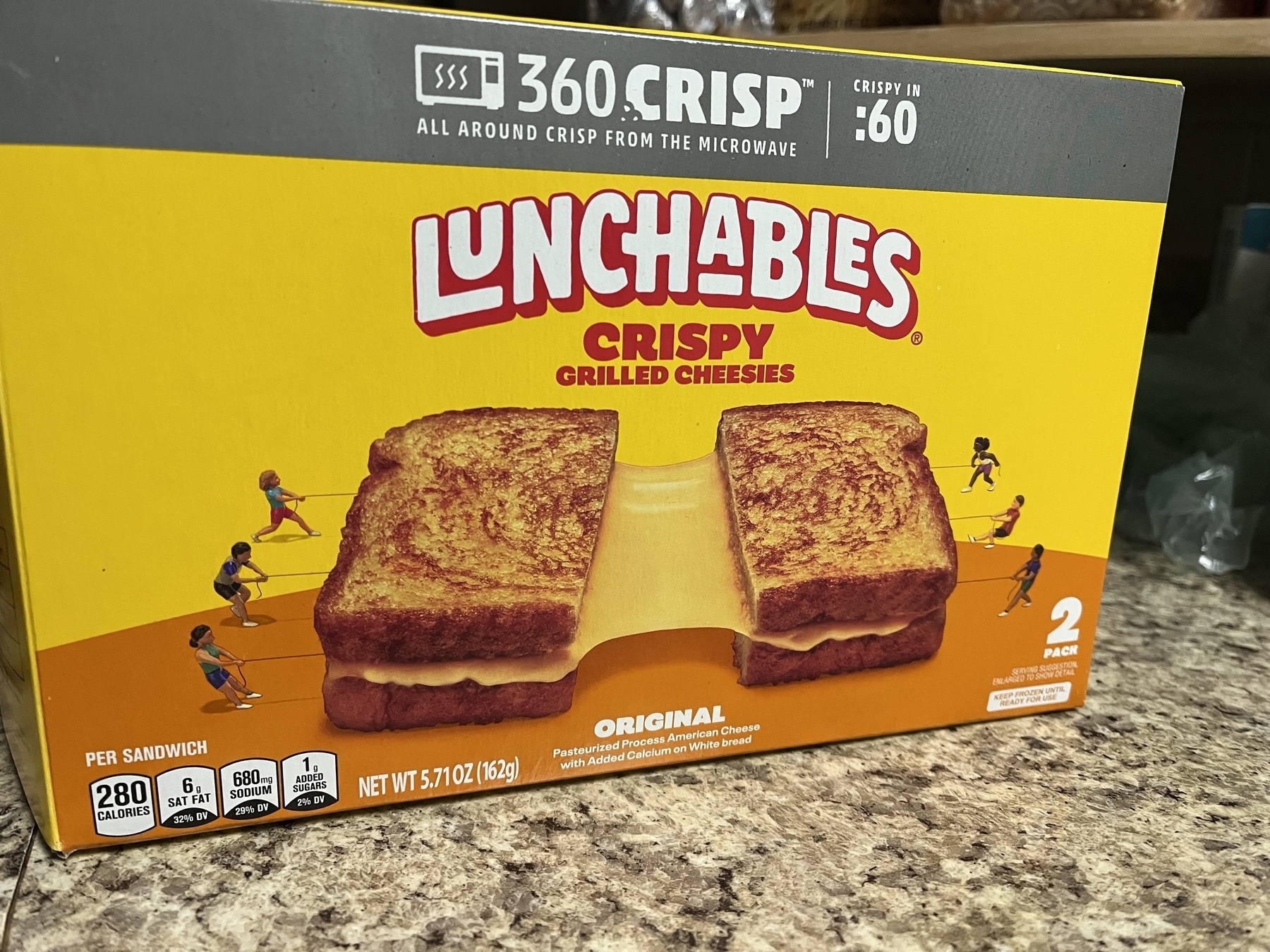 Auto-generated description: A package of Lunchables featuring crispy grilled cheese sandwiches with illustrations of people climbing on the sandwiches.
