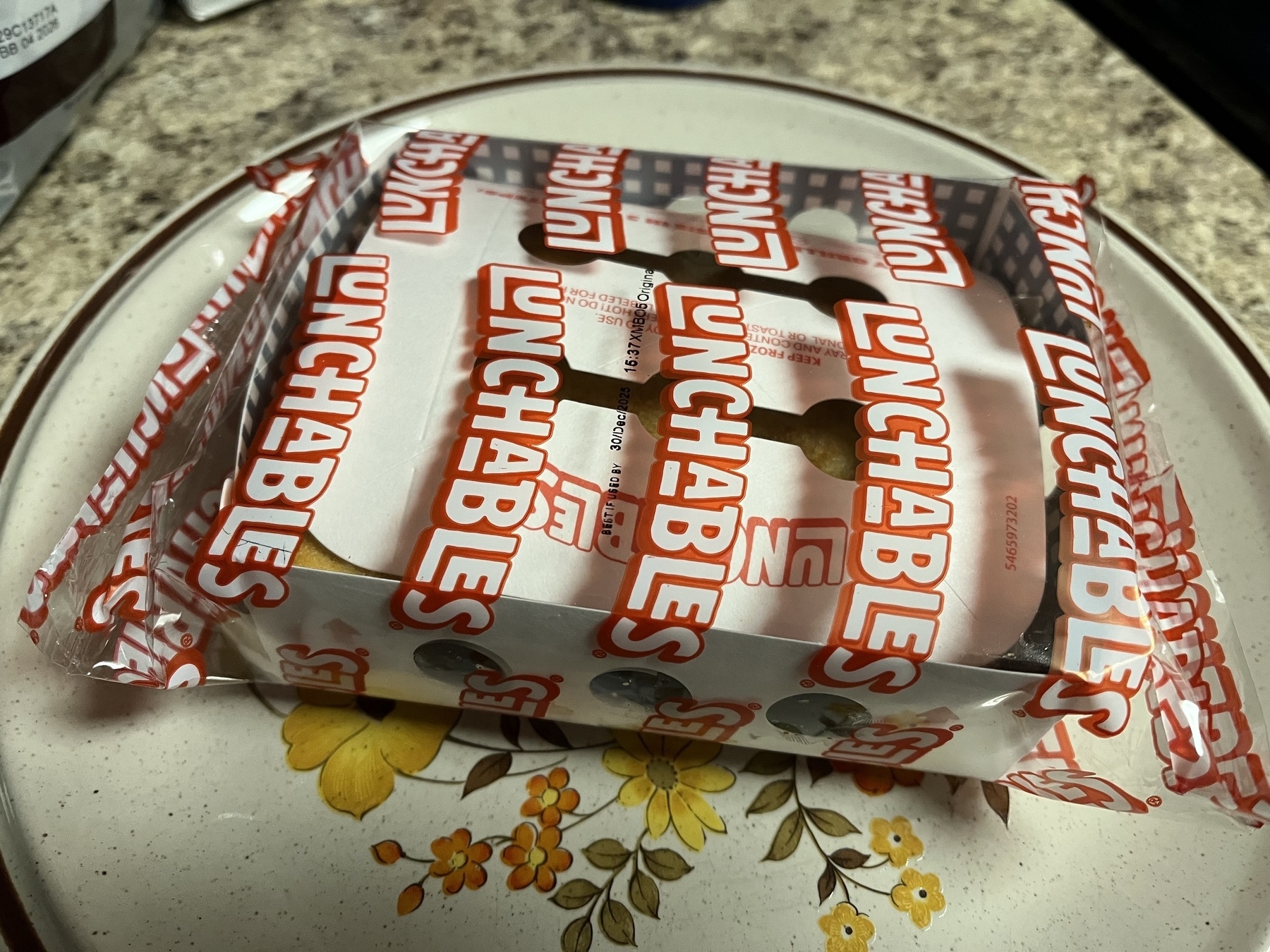 Auto-generated description: A Lunchables package is placed on a plate with a floral design on a speckled countertop.