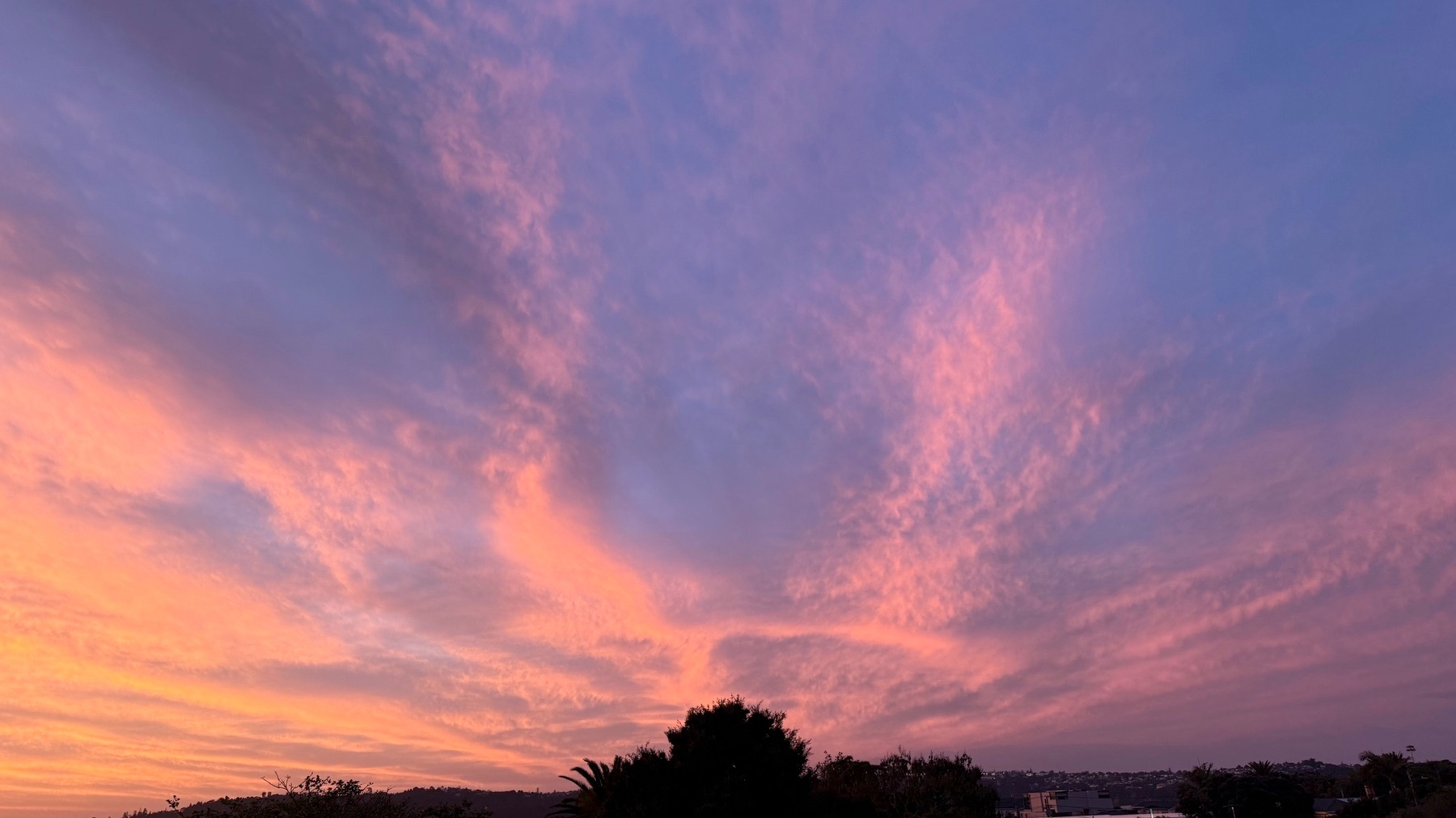 A colorful sky at sunset displays vibrant pink and orange clouds over a silhouetted landscape.