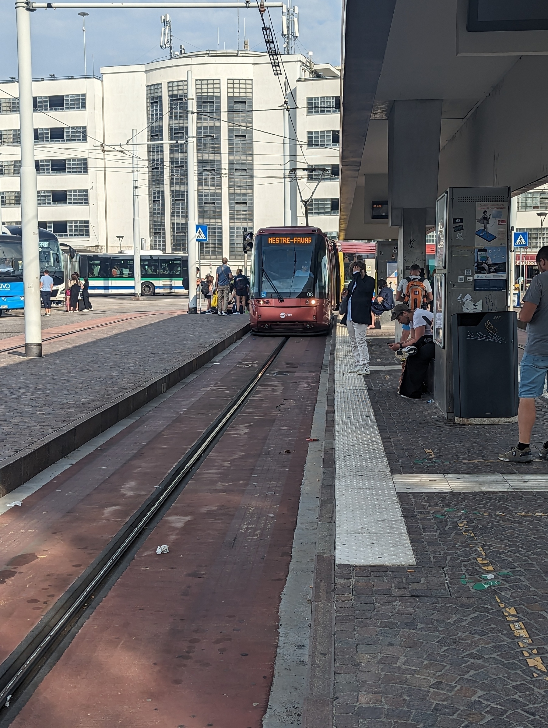 A red tram approaching tram-stop with the track consisting of a single rail.