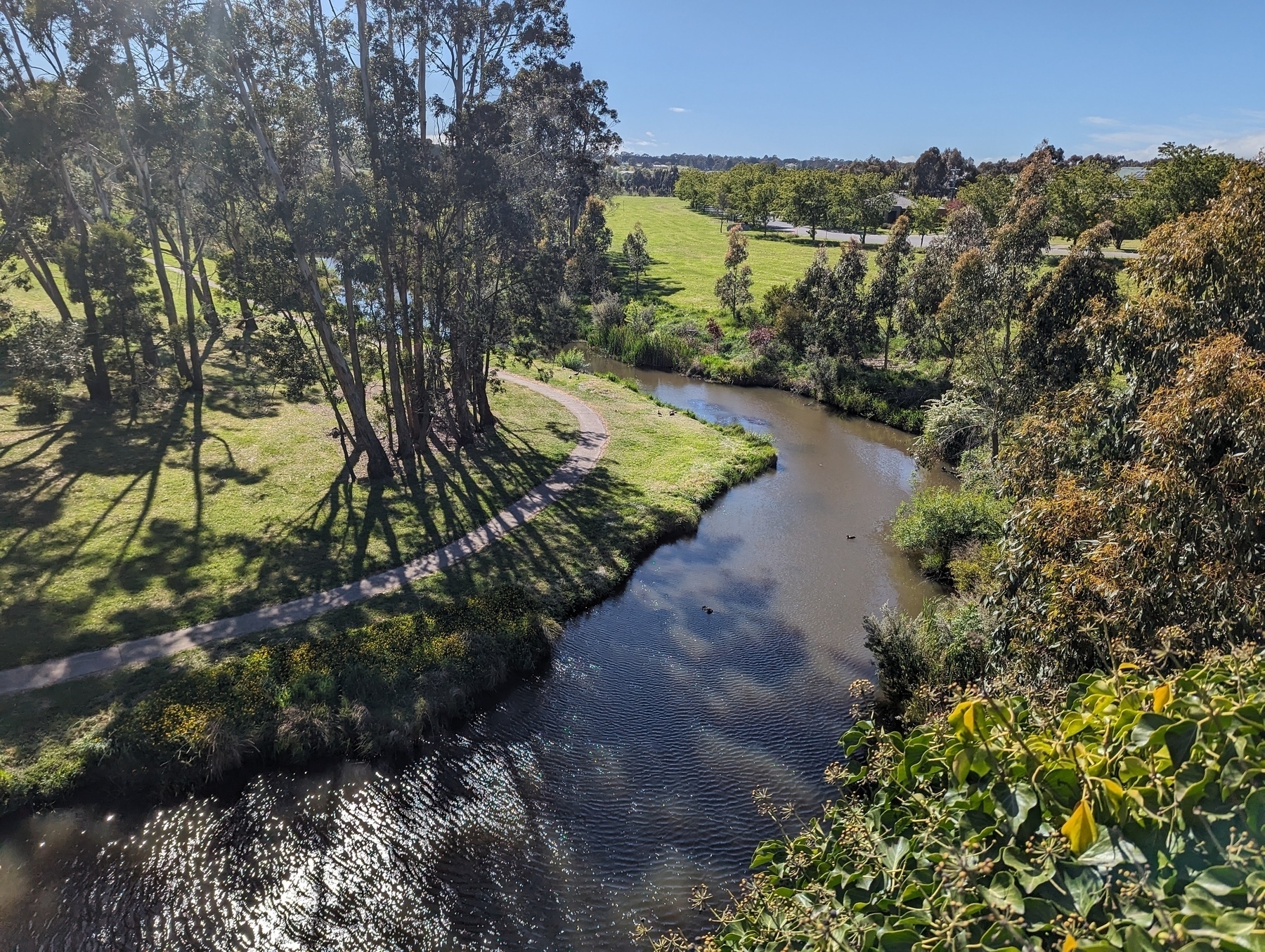 The Campaspe River, twisting towards the Kyneton town under a blue sky. The photo was taken from a bridge.