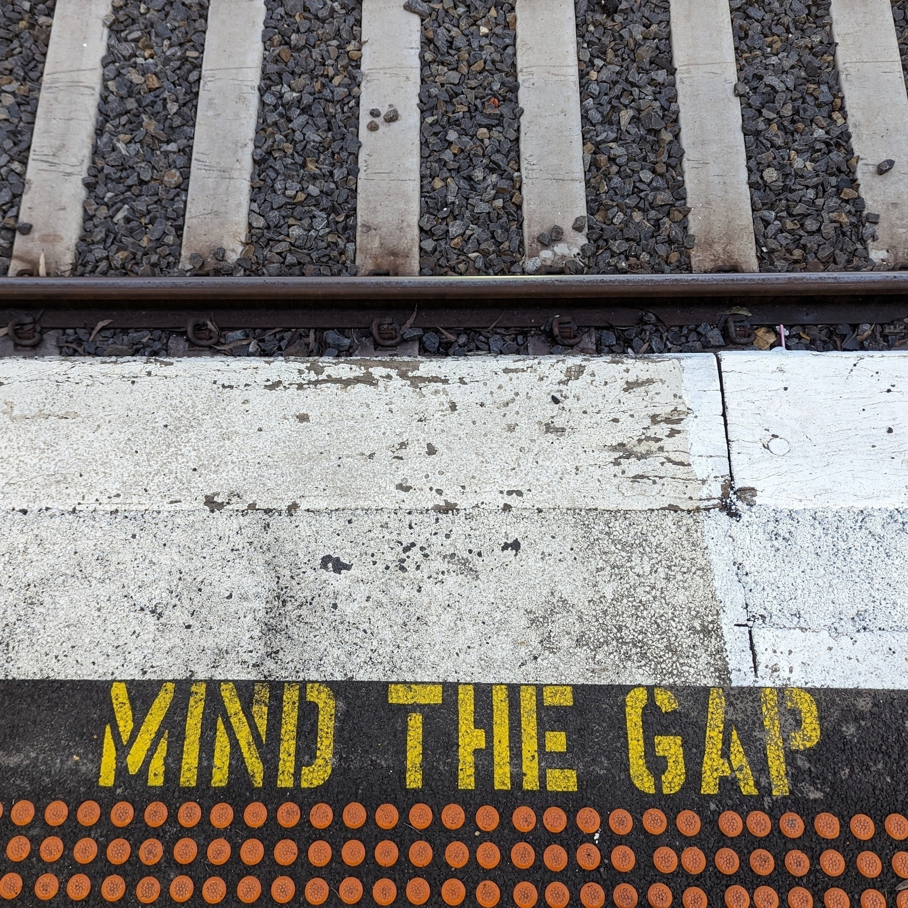 The edge of a train station platform showing part of the rail line and the message Mind the Gap
