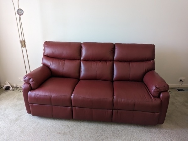 The new couch placed in the living room. The couch is a maroone reclying three seater