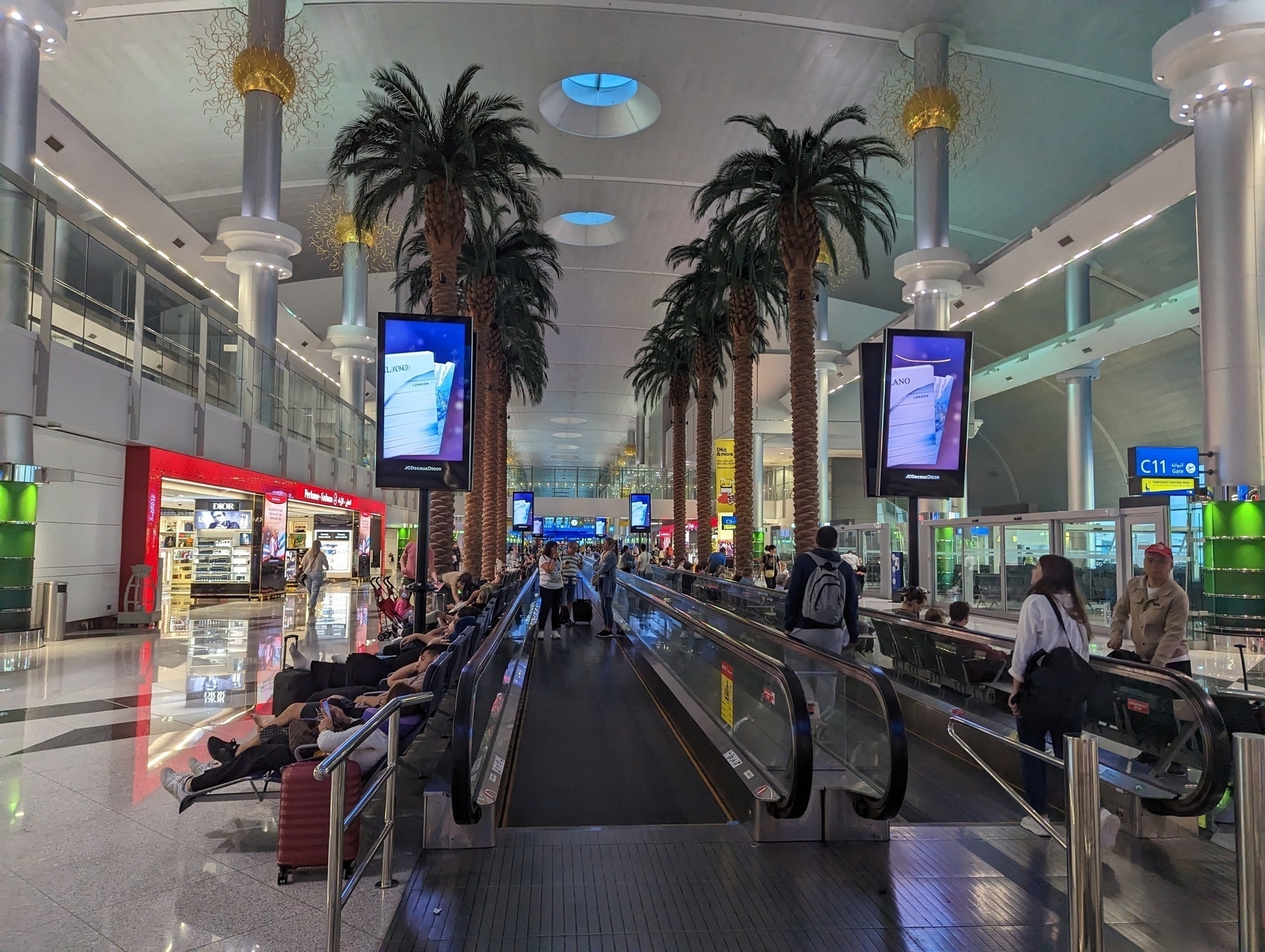 Inside the terminal of Dubai International Airport, looking at palm trees next to a travelator.