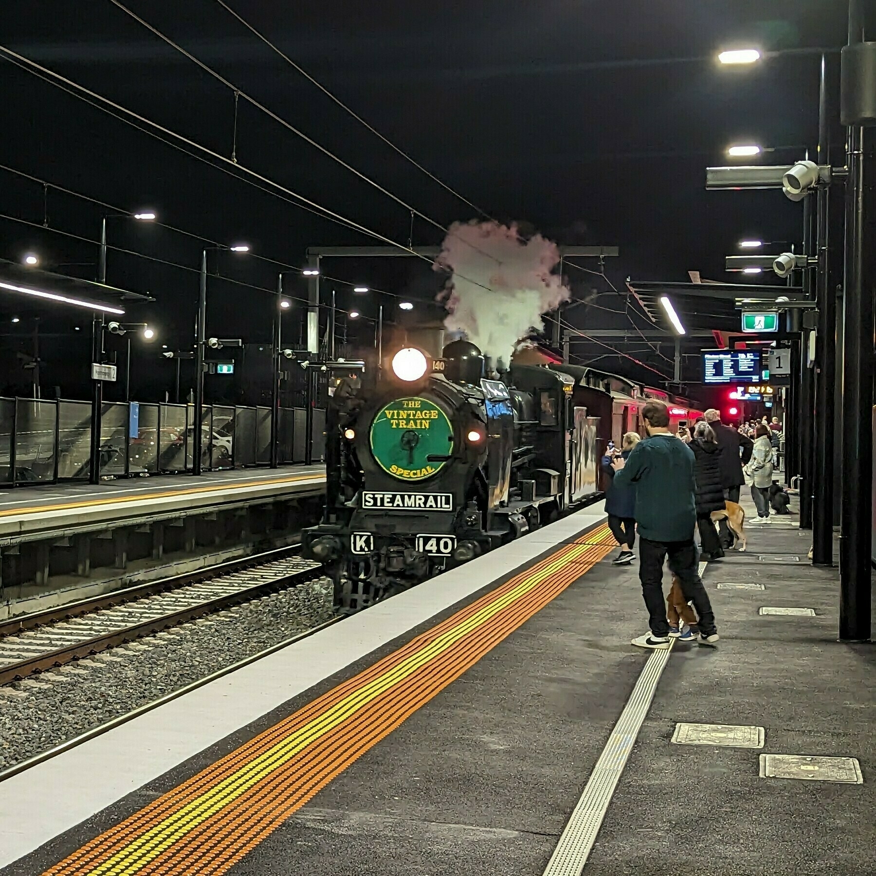 Steam train travelling through station in the evening.