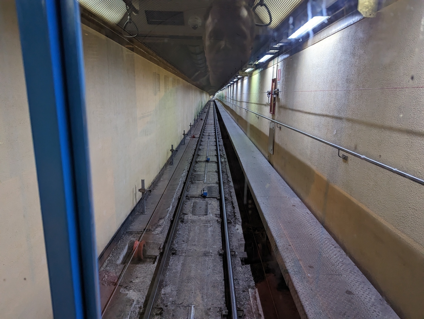 The horizontal section of the lift, which is a corridor with rails heading into the hill and fluorescent lights on the right wall.