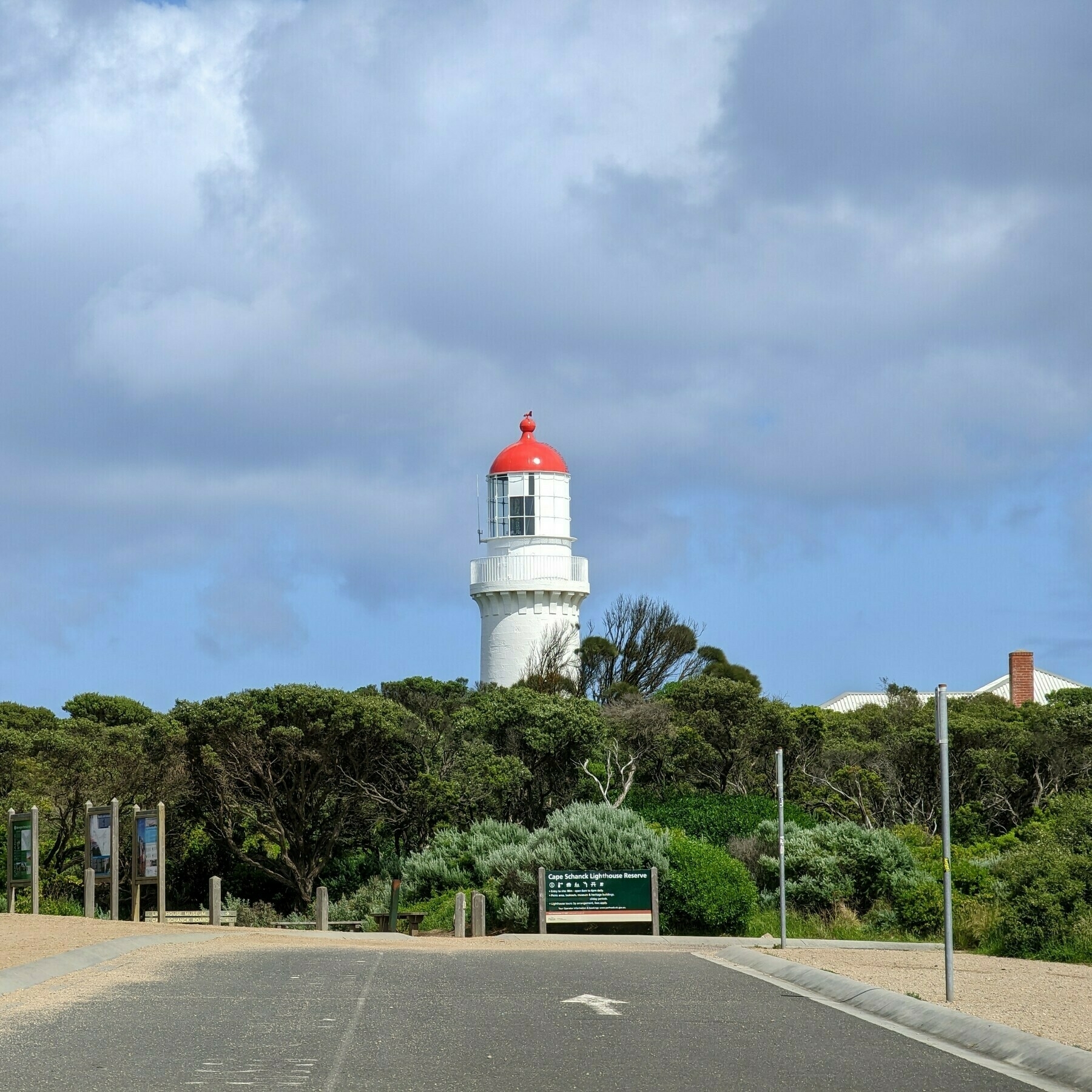 A road in a car park with an arrow pointing to a light-house behind some shrubs