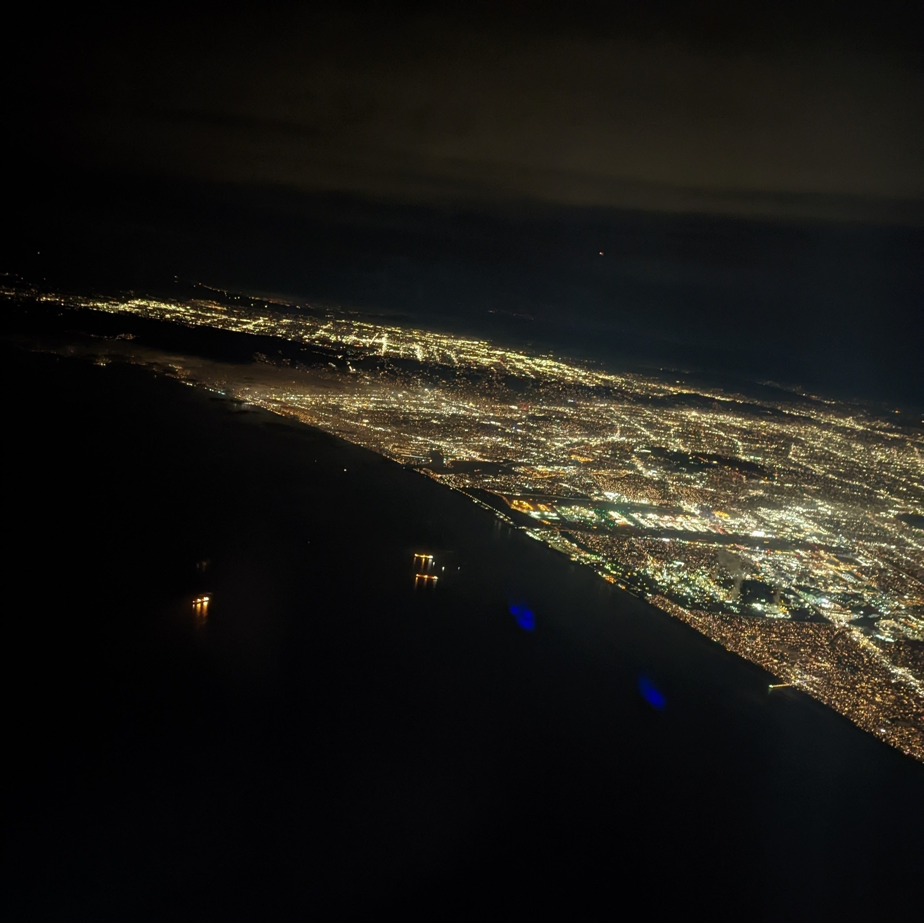 An aeroal photo of a city, Los Angeles, at night; with the city lights contrsting with the darkened bay