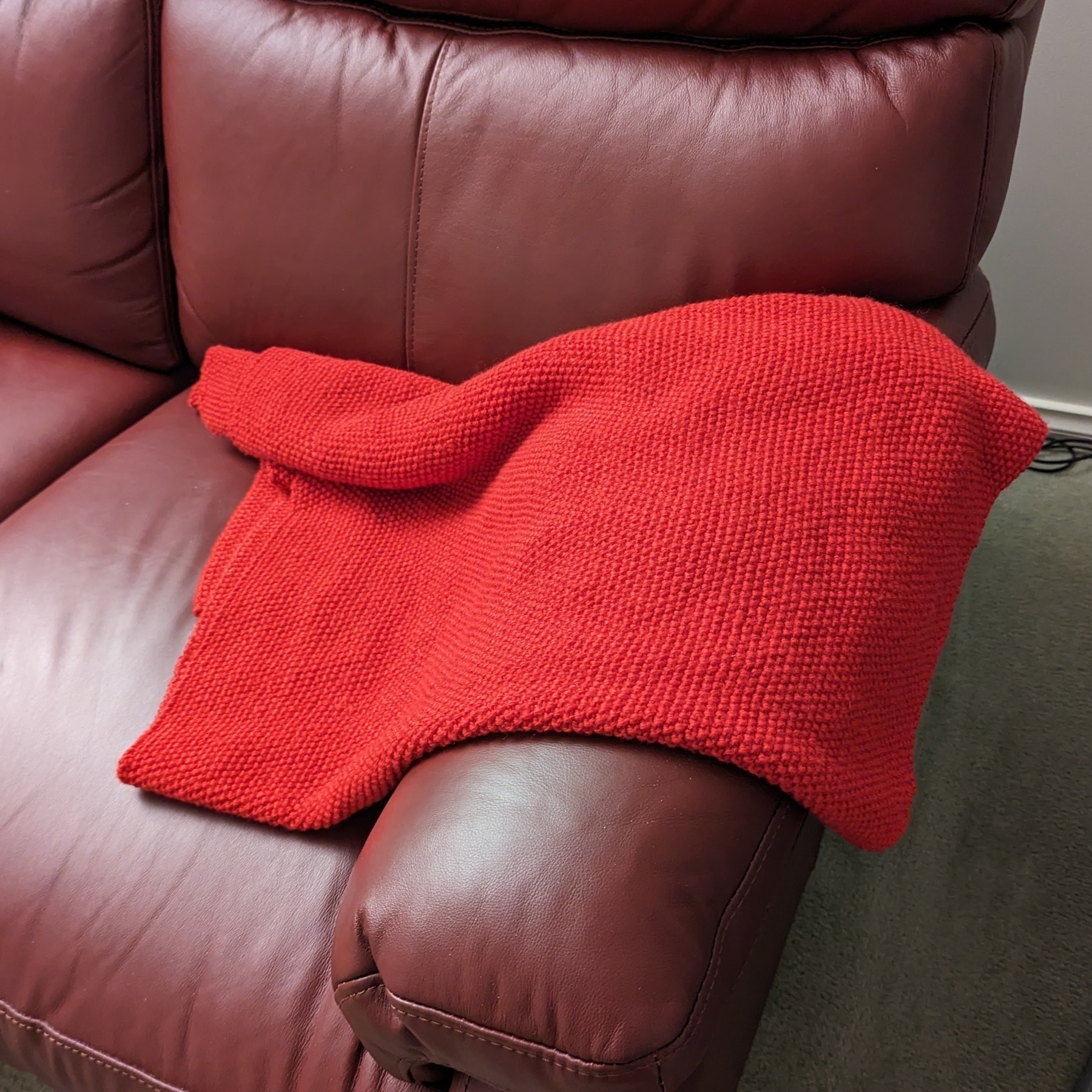 Red blanket draped on the arm of a burgundy couch