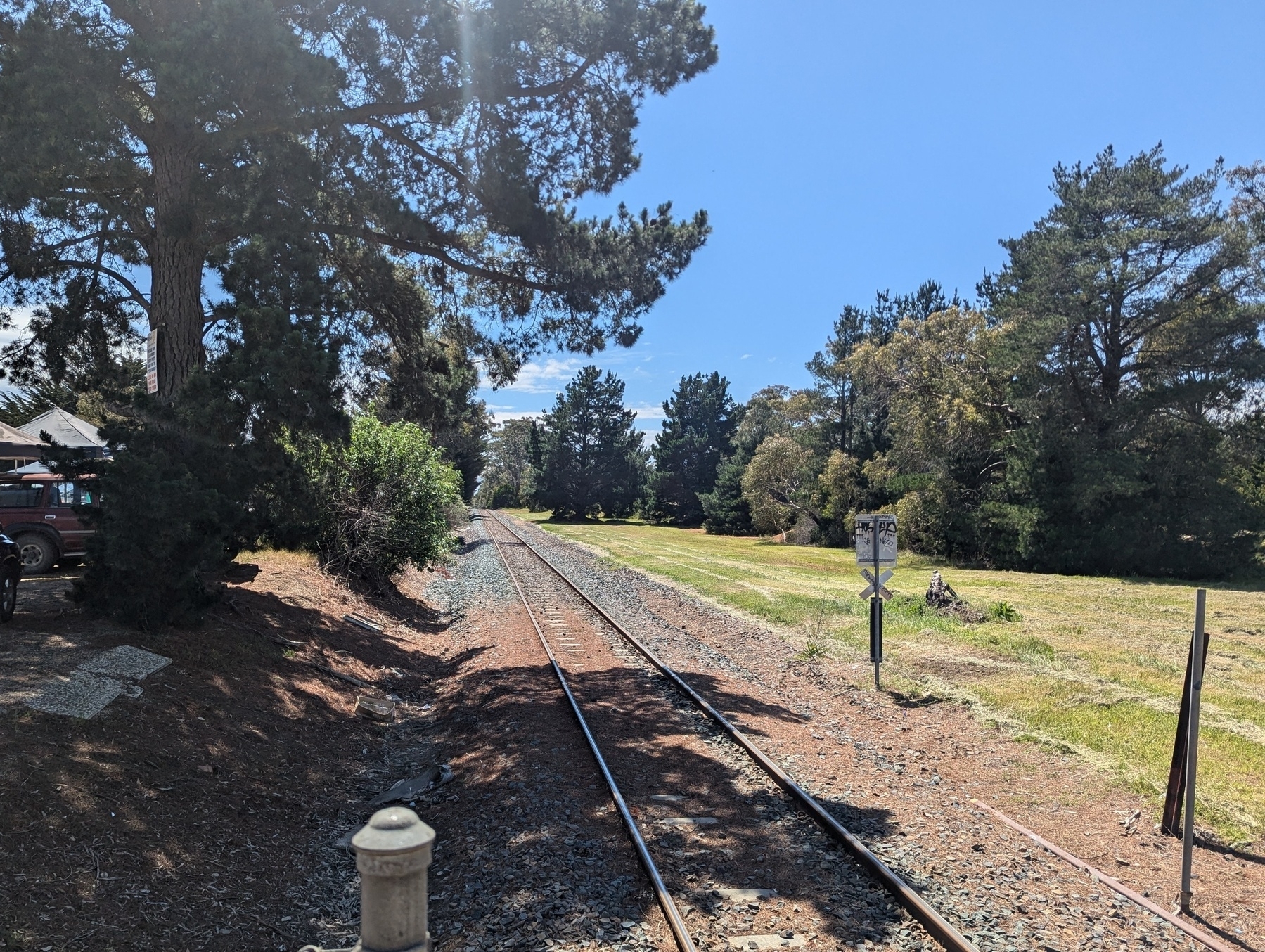 A railway track runs through a scenic landscape with trees and grass under a clear blue sky.