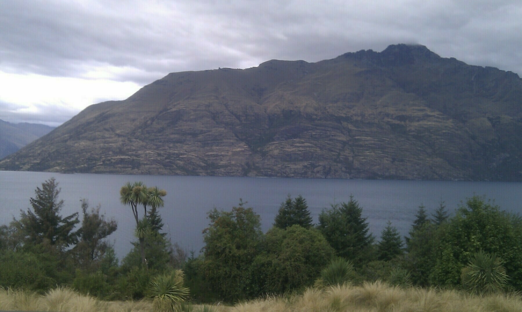 The Remarkables, Queenstown, NZ with a bit of vegetation in the foreground and Lake Wakatipu in the middle.