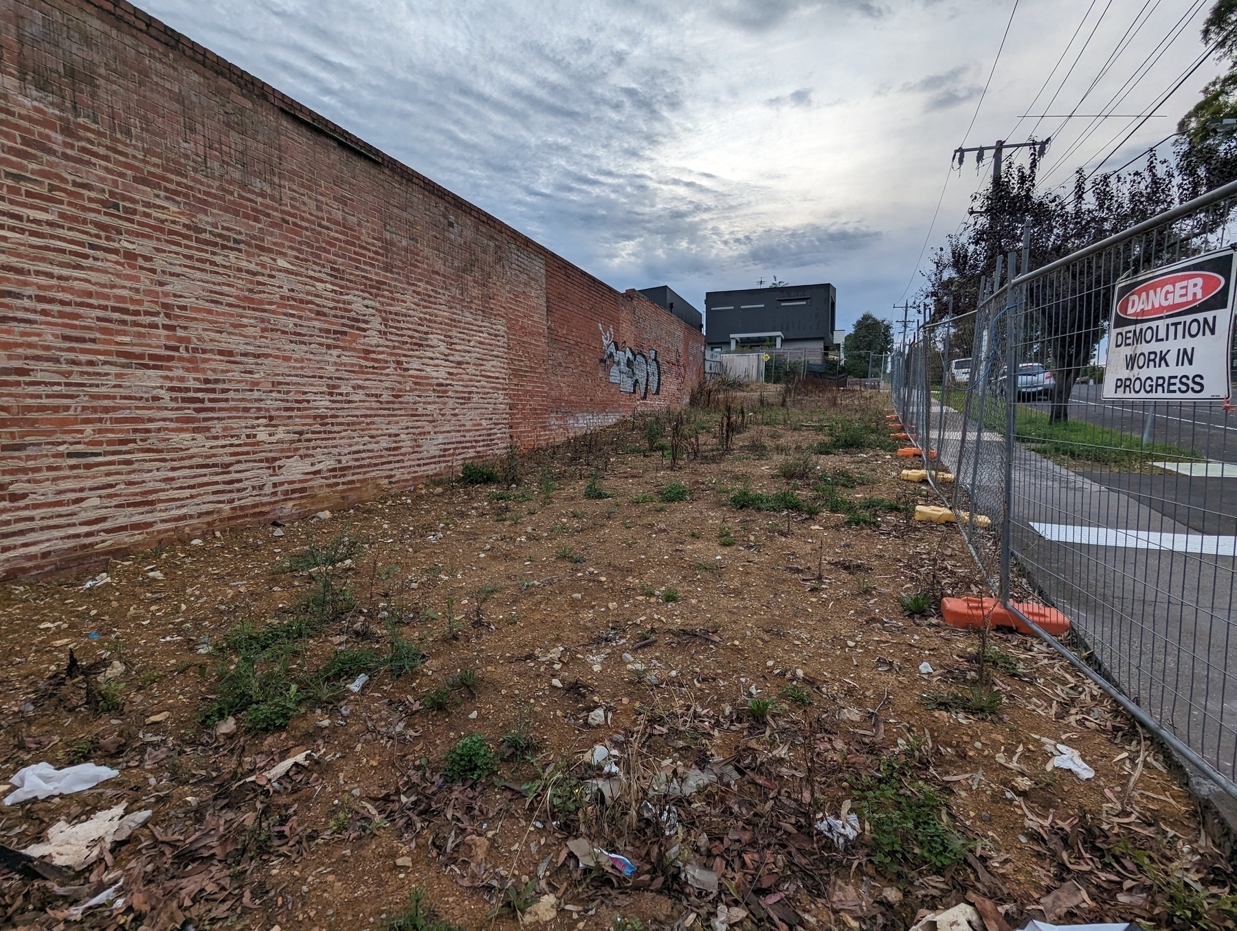 Vacant lot, beside a brick wall and road, where once a building stood.